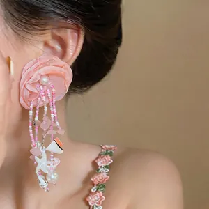 Détail de boucles d'oreilles faites main avec fleur en tissu rose et pompons en perles
