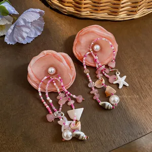 Vue détaillée de boucles d'oreilles fleur en tissu avec franges de coquillages et perles