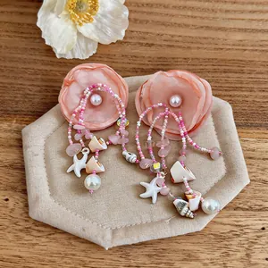 Détail des boucles d'oreilles fleur en tissu rose avec breloques coquillage, étoile et perle.