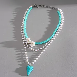 Dettaglio collana di perle multistrato elegante con ciondolo a cuore turchese e fiori.