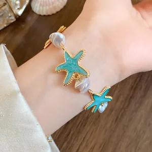 Detail eines goldfarbenen Armbands mit türkisfarbenen Seesternen und weißen Perlen.