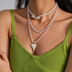 Dettaglio di un girocollo e una collana di perle bianche con ciondolo a cuore crema