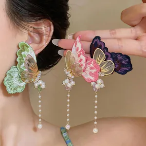 Detailed view of embroidered butterfly earrings with zircons and long pearl tassels.