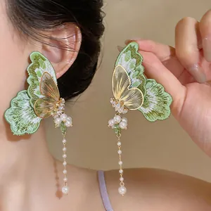 Detail shot of green embroidered butterfly earrings with zircon and long pearl tassels.