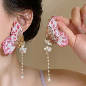 Detailed view of pink embroidered butterfly earrings with long pearl tassels and zircons.