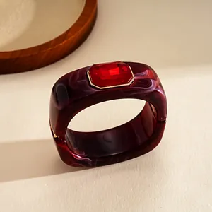 Dettaglio del bracciale quadrato in resina marmorizzata bordeaux con gemma rossa sfaccettata