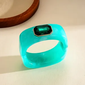 Primo piano di un bracciale in resina turchese con una gemma verde smeraldo.
