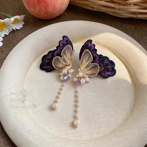 Detailed view of elegant embroidered butterfly earrings with long pearl tassels.