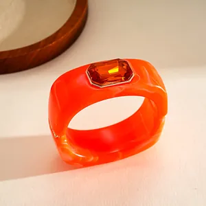 Vista ravvicinata di un bracciale in resina arancione vivace con strass taglio smeraldo.