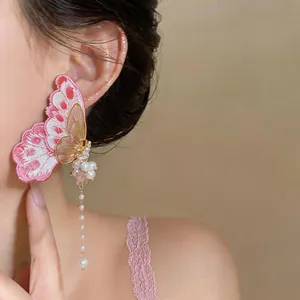 Detailed shot of pink embroidered butterfly earrings with pearl tassels and zircons.