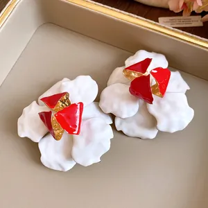 Close-up of retro white flower earrings with red enamel center and gold-tone finish.
