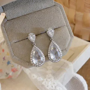 Close-up of elegant pear-shaped zircon drop earrings in a grey velvet jewelry box