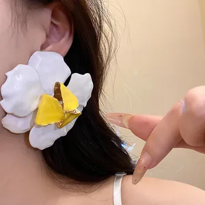 Detailed macro view of large white and yellow enamel flower earrings worn on model