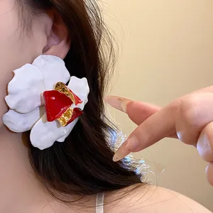 Detail view of an oversized white and red enamel flower earring worn on an ear.