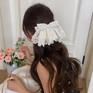 Detailed view of large polka dot bow hair clip with elegant lace trim on model's wavy hair