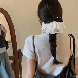 Detailed view of a black polka dot bow hair clip with white lace embroidery.