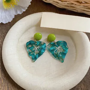 Macro detail view of teal marble swirl resin leaf earrings on a minimalist cream tray