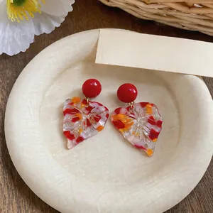Close-up of colorful resin leaf earrings with red studs on a textured plate
