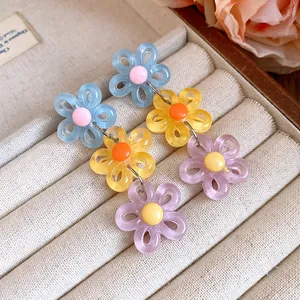 Colorful three-tier acrylic daisy drop earrings presented on a beige velvet jewelry tray.