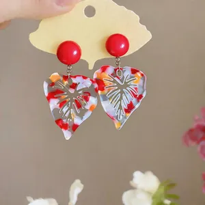 Close-up detail of colorful marbled resin leaf earrings with red studs on a ginkgo card