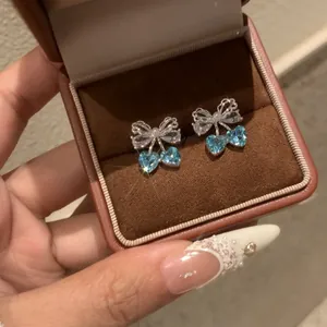 Detailed macro view of silver bow-knot earrings with heart-shaped blue zircon stones