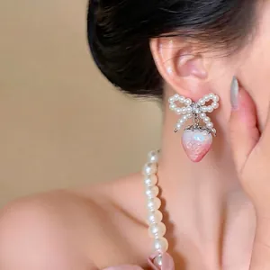 Elegant bow earrings featuring a strawberry pendant and pearls, worn by an Asian model