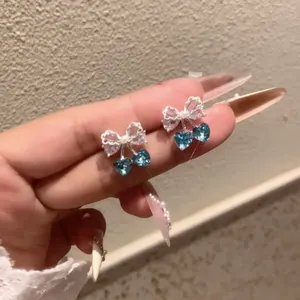 Macro detail of zircon bow-knot earrings featuring heart-shaped blue crystal cherry stones