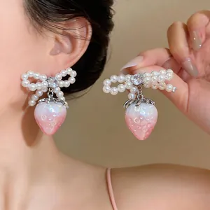 Detail shot of elegant bow earrings featuring pearl accents and a pearlescent strawberry pendant