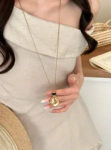 Close-up of Korean style gold wrinkled circular pendant on a long sweater chain