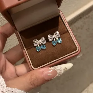Macro view of elegant silver zircon bow earrings with heart-shaped blue stones in a box