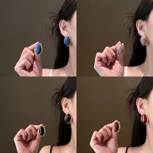 Macro view of vintage style oval stud earrings in blue mauve black and red on model