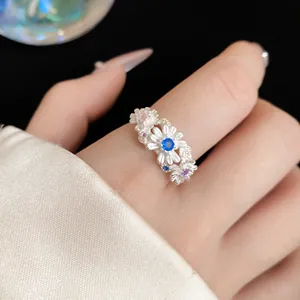 Detail view of a 3D daisy flower ring featuring a vibrant blue center gemstone.