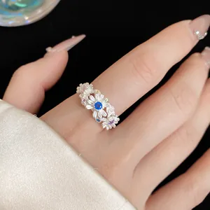 Detailed close-up of a silver daisy ring with blue and purple gemstones on a finger.