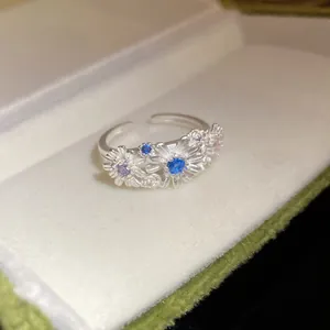 Detailed view of an adjustable daisy ring with vibrant blue and purple stones in a box.