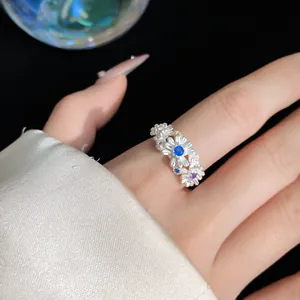 Macro view of a delicate silver daisy flower ring with blue gemstones worn on a finger
