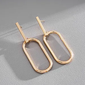 Close-up detail of minimalist gold-tone geometric oval dangle earrings with silver needle