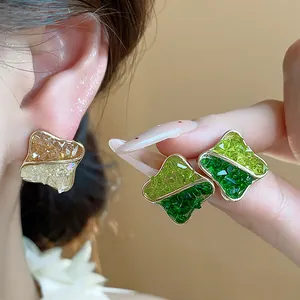 Macro detail of 14K gold plated geometric stud earrings with vibrant crushed green glass