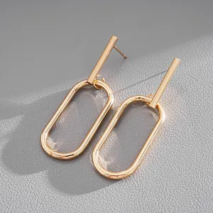 Close-up macro detail of gold oval geometric drop earrings on grey textured surface