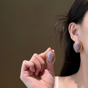 Detail view of vintage oval stud earrings with purple center and gold frame on ear