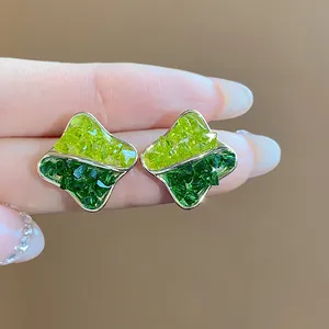 Detailed macro view of geometric 14K gold-plated stud earrings with green crushed glass