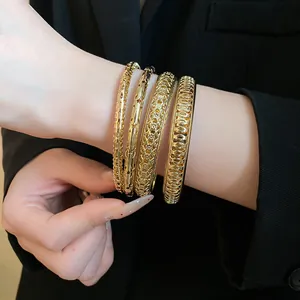 Close-up of four gold geometric textured bangles worn on a wrist with a black blazer.