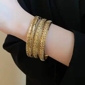 Close-up of a stacked set of four gold geometric bangles with varied textures.