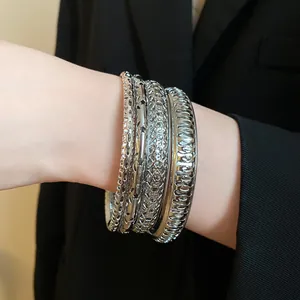 Detailed view of a stacked set of four silver geometric bangles with varied textures on wrist