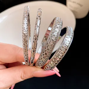 Close-up of four silver-toned textured metal bangles featuring star and geometric patterns.