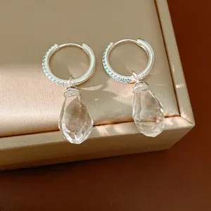 Detail of silver hoop earrings with blue zircon and clear teardrop glass pendants.