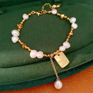 Dettaglio di un bracciale placcato oro 18 carati con perle e ciondolo inciso 'Good Luck'.