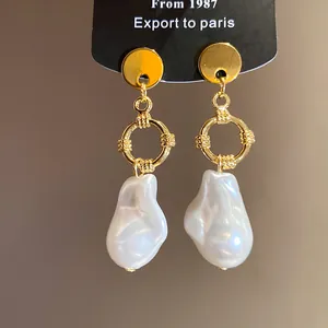 Dettaglio di eleganti orecchini pendenti dorati con perle barocche irregolari