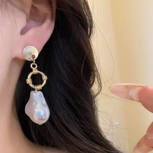 Dettaglio di eleganti orecchini in metallo dorato con perla barocca indossati