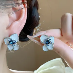 Close-up detail of white enamel flower stud earrings featuring a deep blue crystal center.