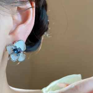 Macro detail showing an elegant flower stud earring with blue crystal and white petals